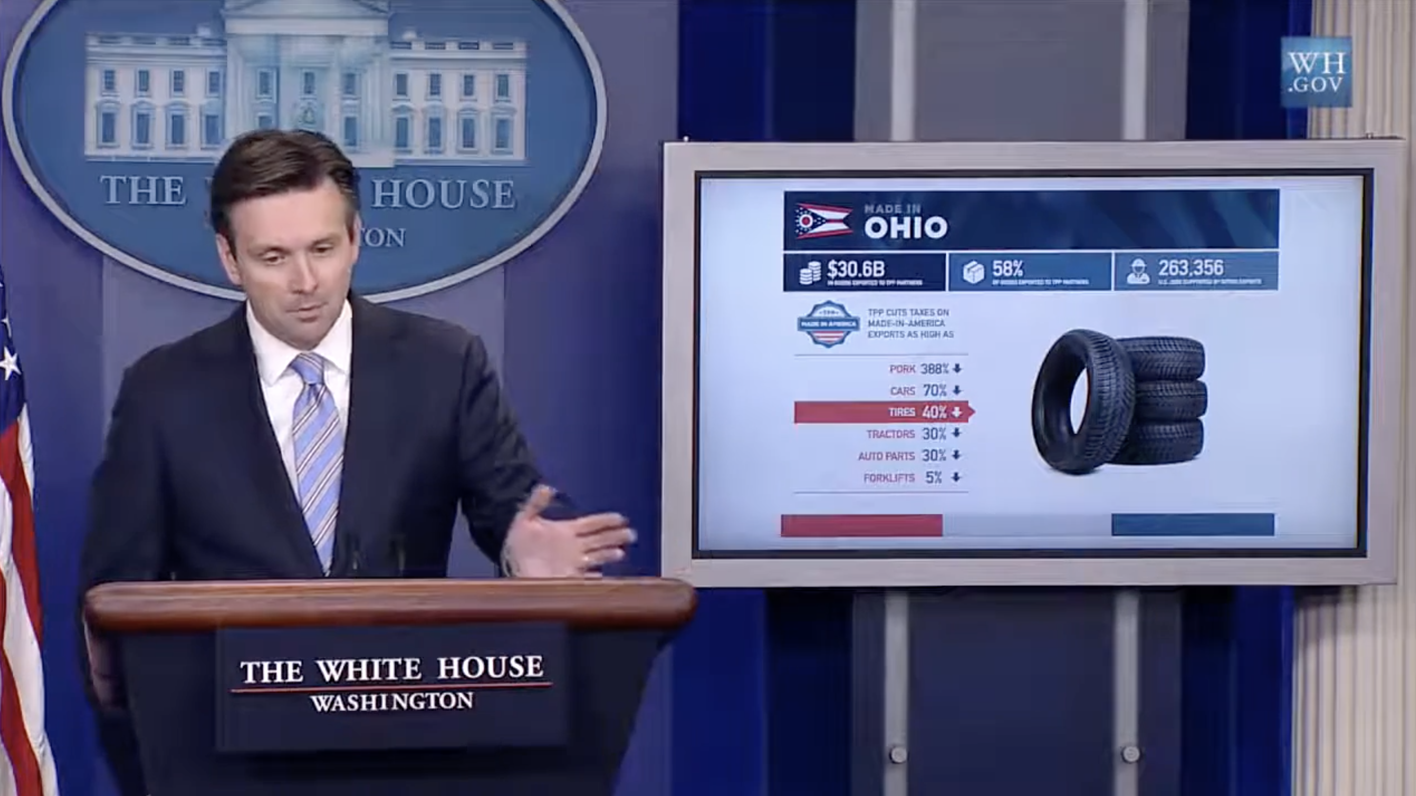 Still from a White House press room briefing recording of former Press Secretary Josh Earnest giving a presentation on the Trans-Pacific Partnership with a page from the booklet displayed on a TV screen.